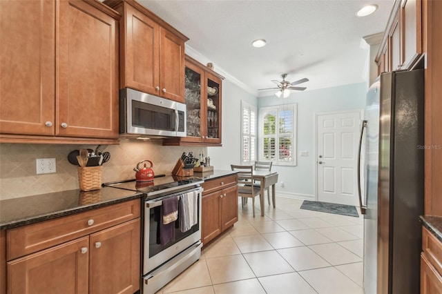 kitchen with light tile patterned floors, tasteful backsplash, appliances with stainless steel finishes, brown cabinets, and crown molding