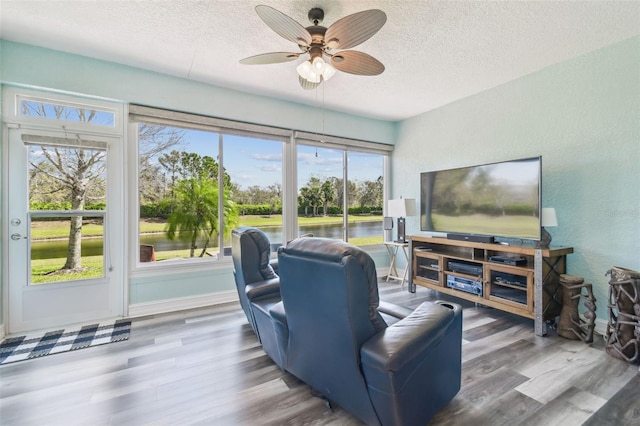 living area with a textured wall, a textured ceiling, baseboards, and wood finished floors