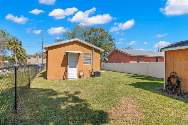 back of property with central AC unit, a fenced backyard, an outdoor structure, a yard, and stucco siding