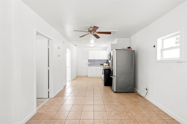 kitchen with light tile patterned floors, tasteful backsplash, light countertops, freestanding refrigerator, and white cabinets