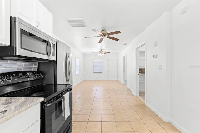 kitchen featuring light tile patterned floors, stainless steel microwave, black range with electric stovetop, visible vents, and white cabinets