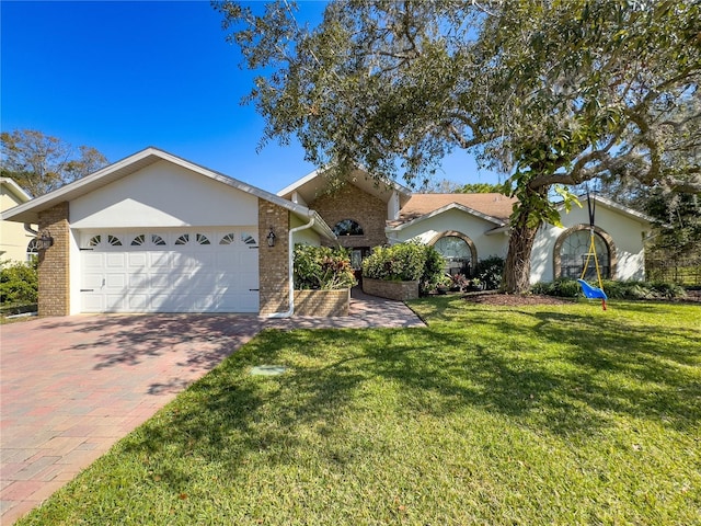 ranch-style home featuring a garage, brick siding, decorative driveway, a front lawn, and stucco siding