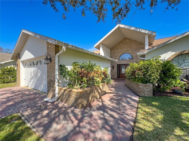 ranch-style home with a garage, brick siding, decorative driveway, and stucco siding