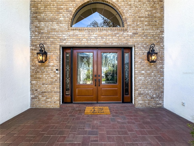 entrance to property with brick siding, stucco siding, and french doors