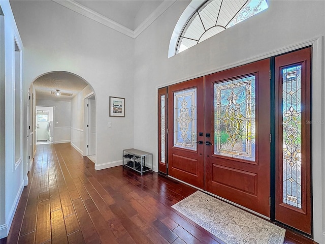 foyer featuring arched walkways, crown molding, dark wood finished floors, a towering ceiling, and baseboards