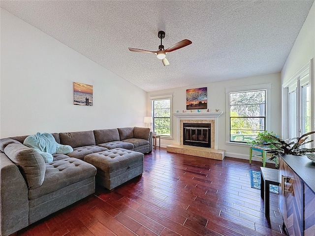 living area featuring ceiling fan, a textured ceiling, dark wood-style flooring, vaulted ceiling, and a glass covered fireplace