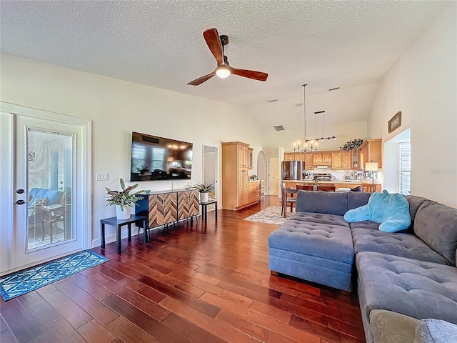 living room featuring a textured ceiling, ceiling fan with notable chandelier, visible vents, vaulted ceiling, and dark wood-style floors