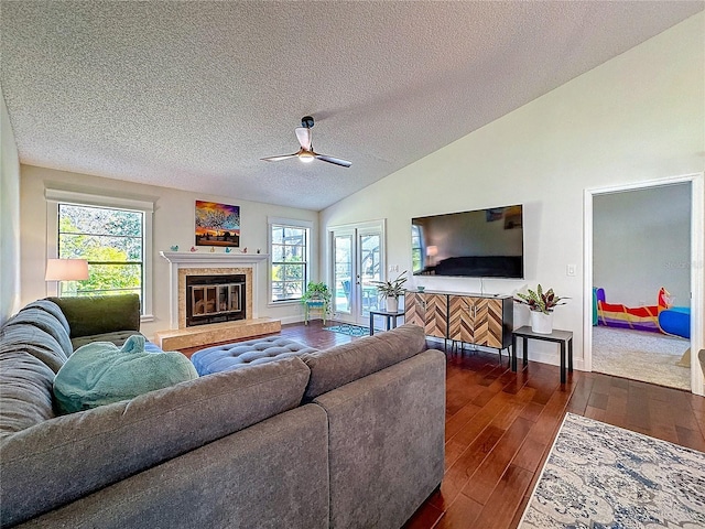 living room featuring a healthy amount of sunlight, vaulted ceiling, dark wood-type flooring, and a tile fireplace