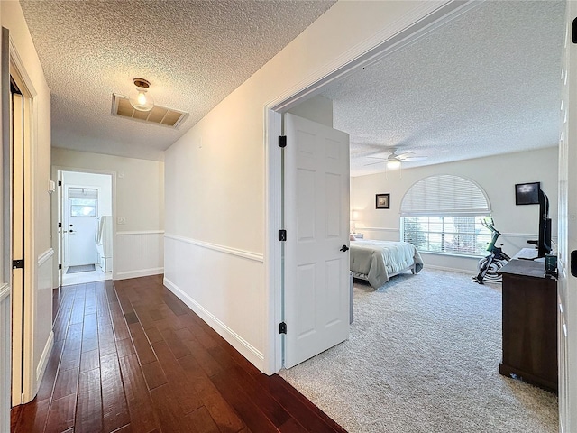 hall featuring baseboards, a textured ceiling, visible vents, and wood finished floors