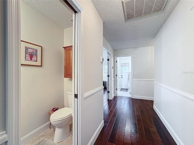 hall featuring dark wood-style flooring, visible vents, a textured ceiling, and baseboards