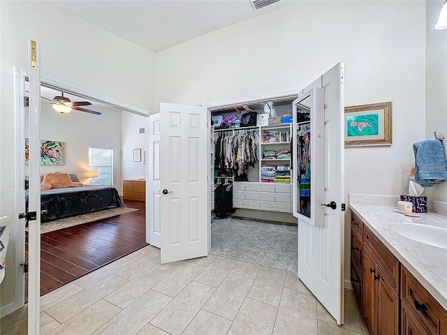 bathroom with a walk in closet, visible vents, connected bathroom, vanity, and ceiling fan