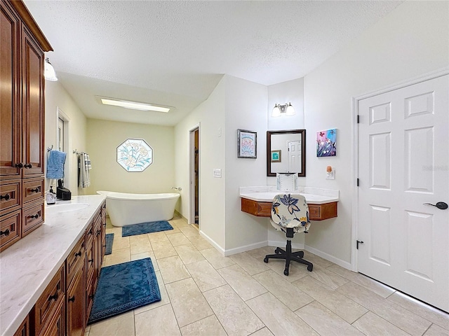 bathroom with a sink, a textured ceiling, tile patterned flooring, a freestanding tub, and baseboards