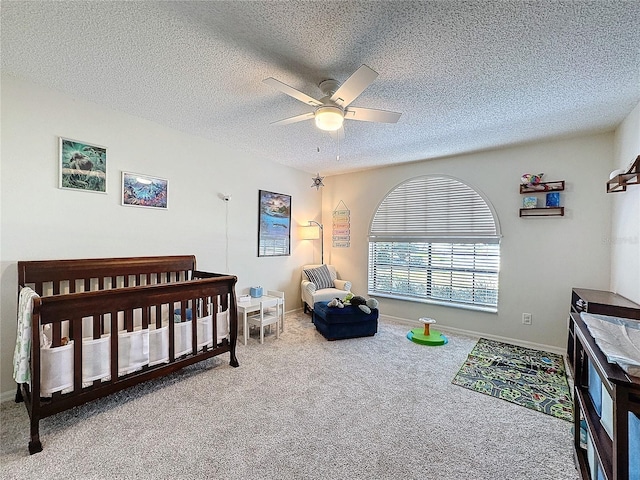 bedroom with carpet floors, a ceiling fan, a textured ceiling, a nursery area, and baseboards