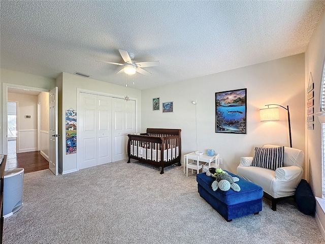 bedroom featuring ceiling fan, a textured ceiling, visible vents, a closet, and carpet