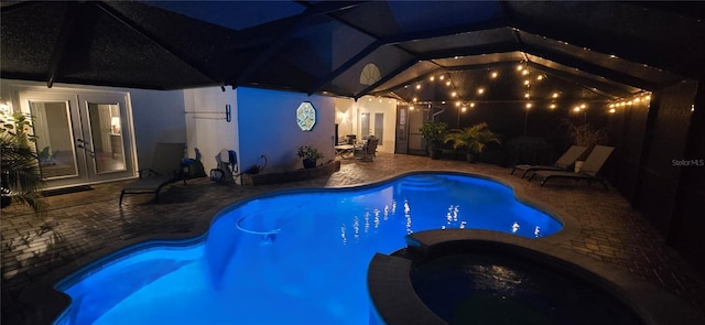 pool at night featuring a patio area, a pool with connected hot tub, glass enclosure, and french doors