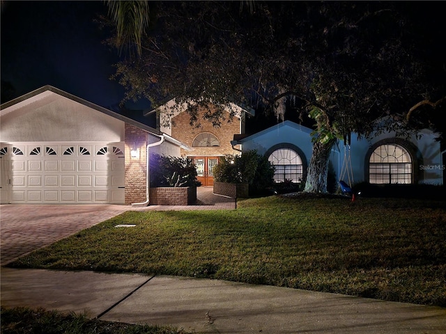 view of front of house featuring decorative driveway, brick siding, stucco siding, a lawn, and a garage