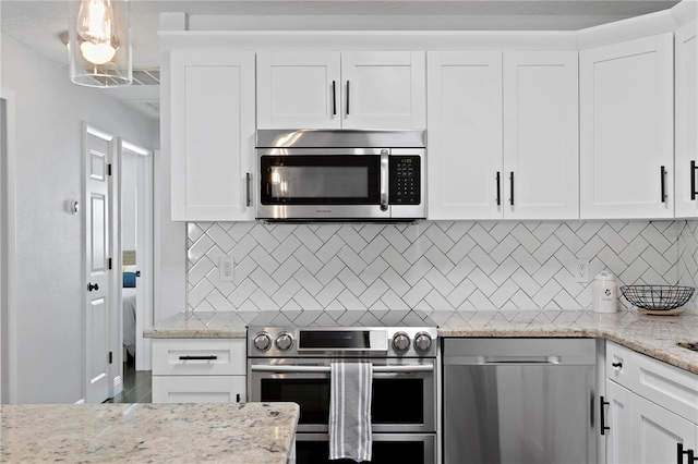 kitchen featuring stainless steel appliances, white cabinetry, light stone countertops, and backsplash