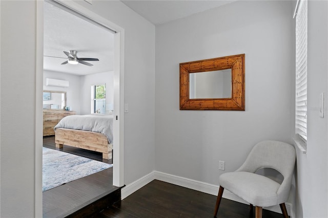 sitting room featuring a wall mounted AC, dark wood finished floors, baseboards, and a ceiling fan