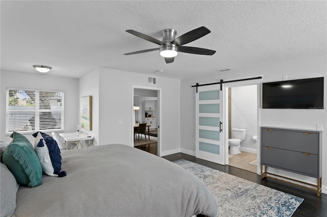 bedroom featuring a barn door, dark wood-type flooring, baseboards, a textured ceiling, and ensuite bathroom