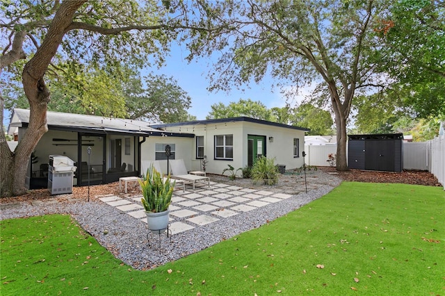 rear view of property with a sunroom, a patio area, stucco siding, a storage shed, and an outdoor structure