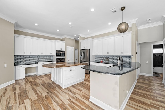 kitchen with visible vents, dark stone counters, a peninsula, stainless steel refrigerator with ice dispenser, and a sink