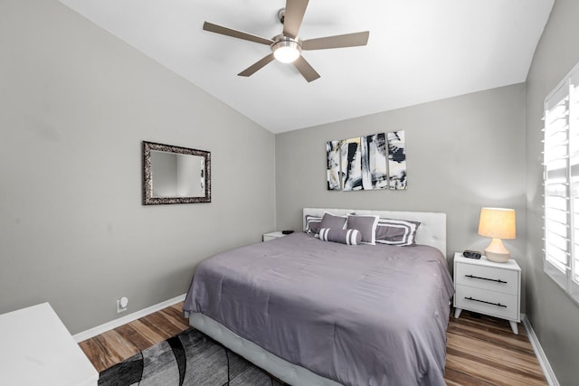 bedroom with multiple windows, vaulted ceiling, baseboards, and wood finished floors