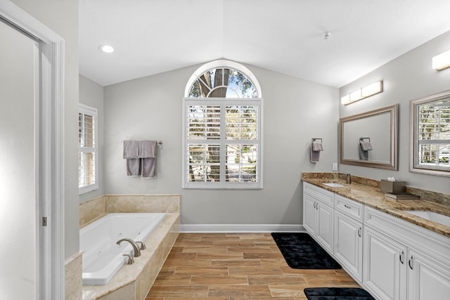 bathroom with double vanity, baseboards, a jetted tub, vaulted ceiling, and a sink