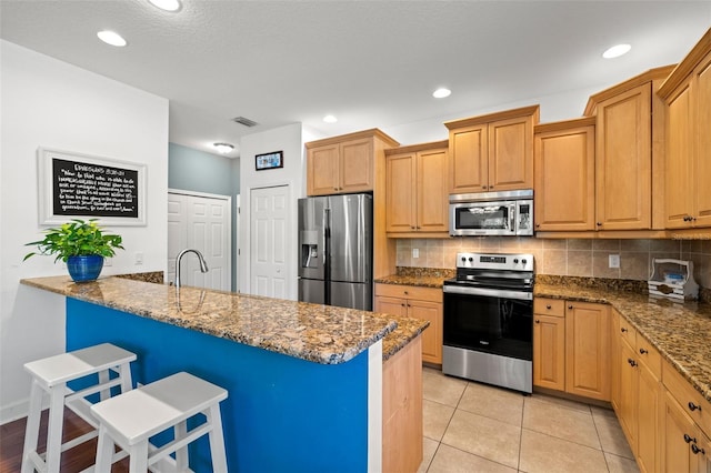 kitchen featuring stainless steel appliances, dark stone countertops, backsplash, and a breakfast bar area