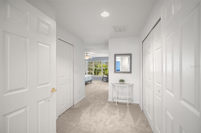 hall featuring baseboards, visible vents, and light colored carpet