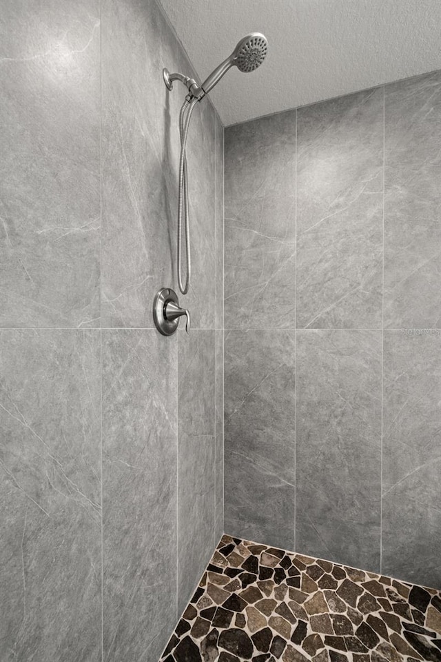 bathroom with stone finish flooring, a textured ceiling, and tiled shower