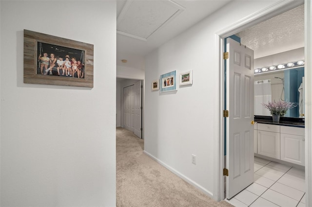 hallway with attic access, light carpet, baseboards, and light tile patterned flooring