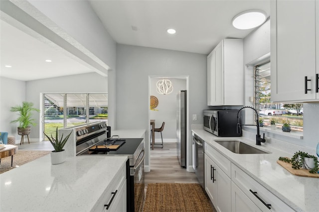 kitchen with appliances with stainless steel finishes, light stone counters, wood finished floors, white cabinetry, and a sink