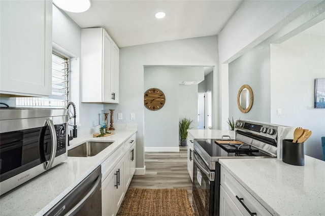 kitchen with stainless steel appliances, white cabinets, a sink, and light stone countertops