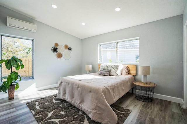 bedroom featuring multiple windows, a wall unit AC, wood finished floors, and baseboards