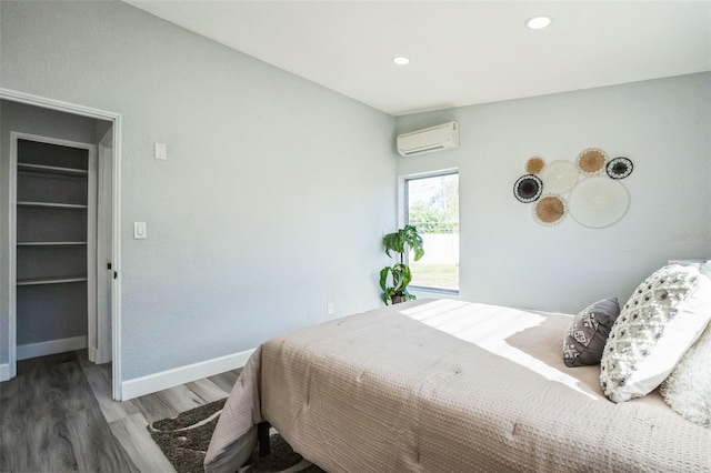 bedroom featuring baseboards, wood finished floors, a wall mounted air conditioner, a spacious closet, and recessed lighting