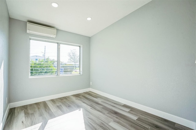 unfurnished room featuring recessed lighting, a wall unit AC, baseboards, and wood finished floors