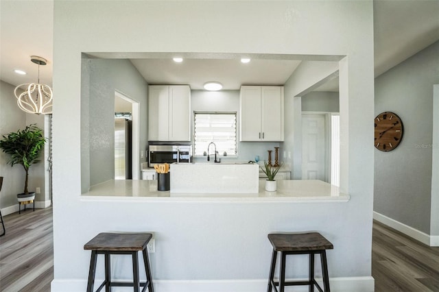 kitchen featuring white cabinets, a breakfast bar, wood finished floors, a peninsula, and stainless steel appliances