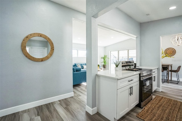 kitchen with wood finished floors, white cabinetry, baseboards, light countertops, and stainless steel electric stove