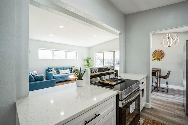 kitchen with light stone counters, stainless steel electric stove, white cabinetry, wood finished floors, and baseboards