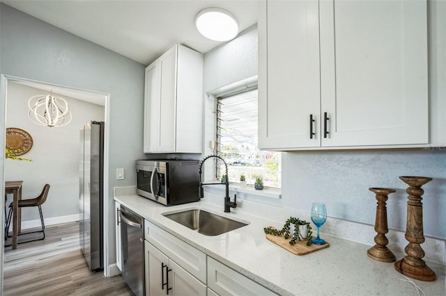 kitchen featuring a sink, white cabinets, appliances with stainless steel finishes, light stone countertops, and light wood finished floors