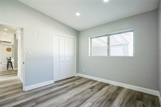 unfurnished bedroom featuring baseboards, lofted ceiling, wood finished floors, a wall mounted air conditioner, and recessed lighting