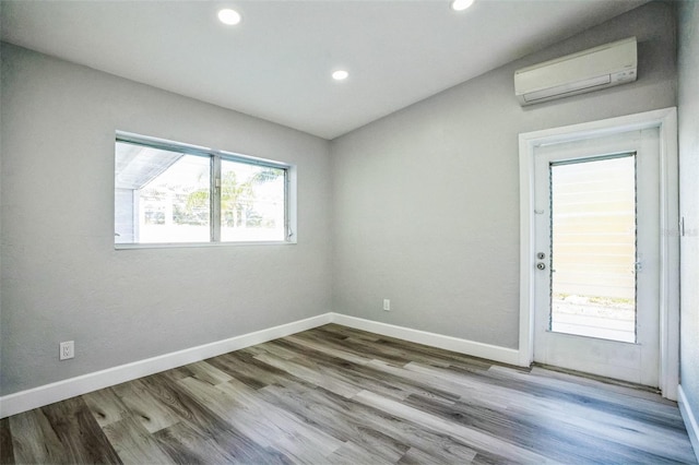 empty room featuring recessed lighting, wood finished floors, baseboards, and a wall mounted AC