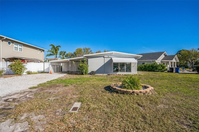 rear view of house featuring gravel driveway, a lawn, fence, and a carport