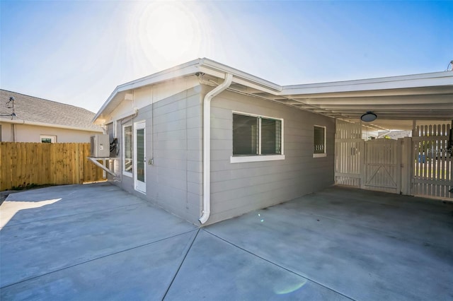 view of property exterior featuring a carport, a patio, fence, and a gate