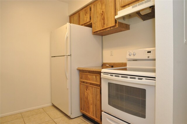 kitchen with light tile patterned floors, under cabinet range hood, white appliances, baseboards, and brown cabinets