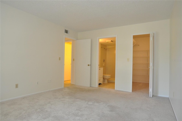 unfurnished bedroom featuring light carpet, visible vents, a spacious closet, a textured ceiling, and a closet