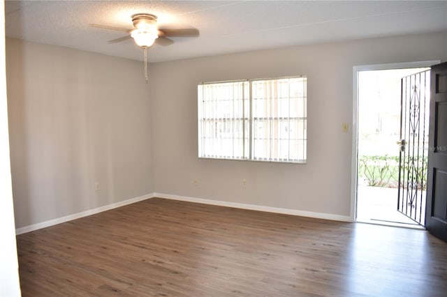 empty room with a textured ceiling, wood finished floors, a ceiling fan, and baseboards