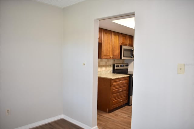 kitchen with brown cabinets, light wood-style floors, stainless steel appliances, and backsplash