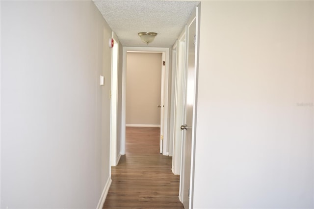 corridor with a textured ceiling, dark wood finished floors, and baseboards