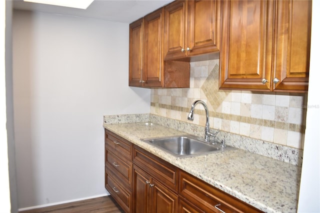 kitchen with light stone countertops, backsplash, a sink, and brown cabinetry